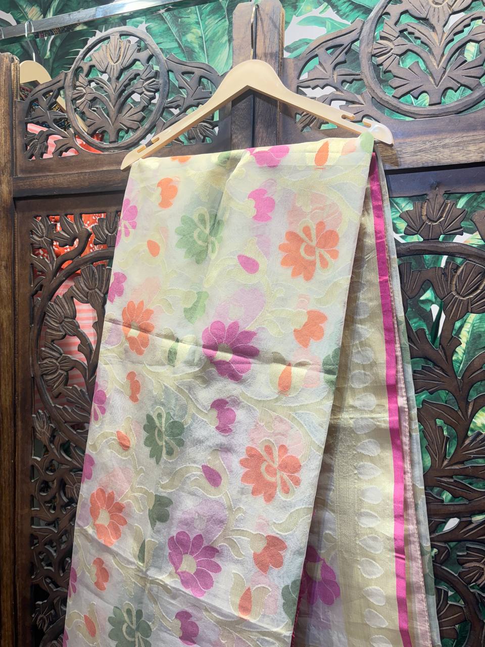Floral-patterned fabric draped over a wooden hanger against an ornate wooden background