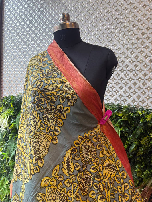 A close-up shot of the grey and yellow Kalamkari dupatta draped on a mannequin, highlighting the texture and the rich rust-orange Nijam border.