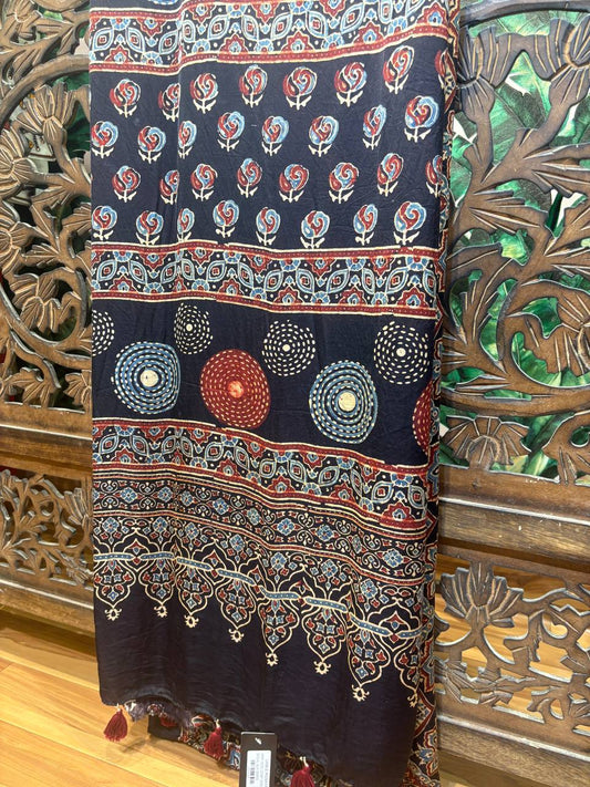 Full view of the Ishani Ajrakh Hand Block Printed Modal Silk Saree in indigo and maroon, hanging on a hanger against a carved wooden screen.