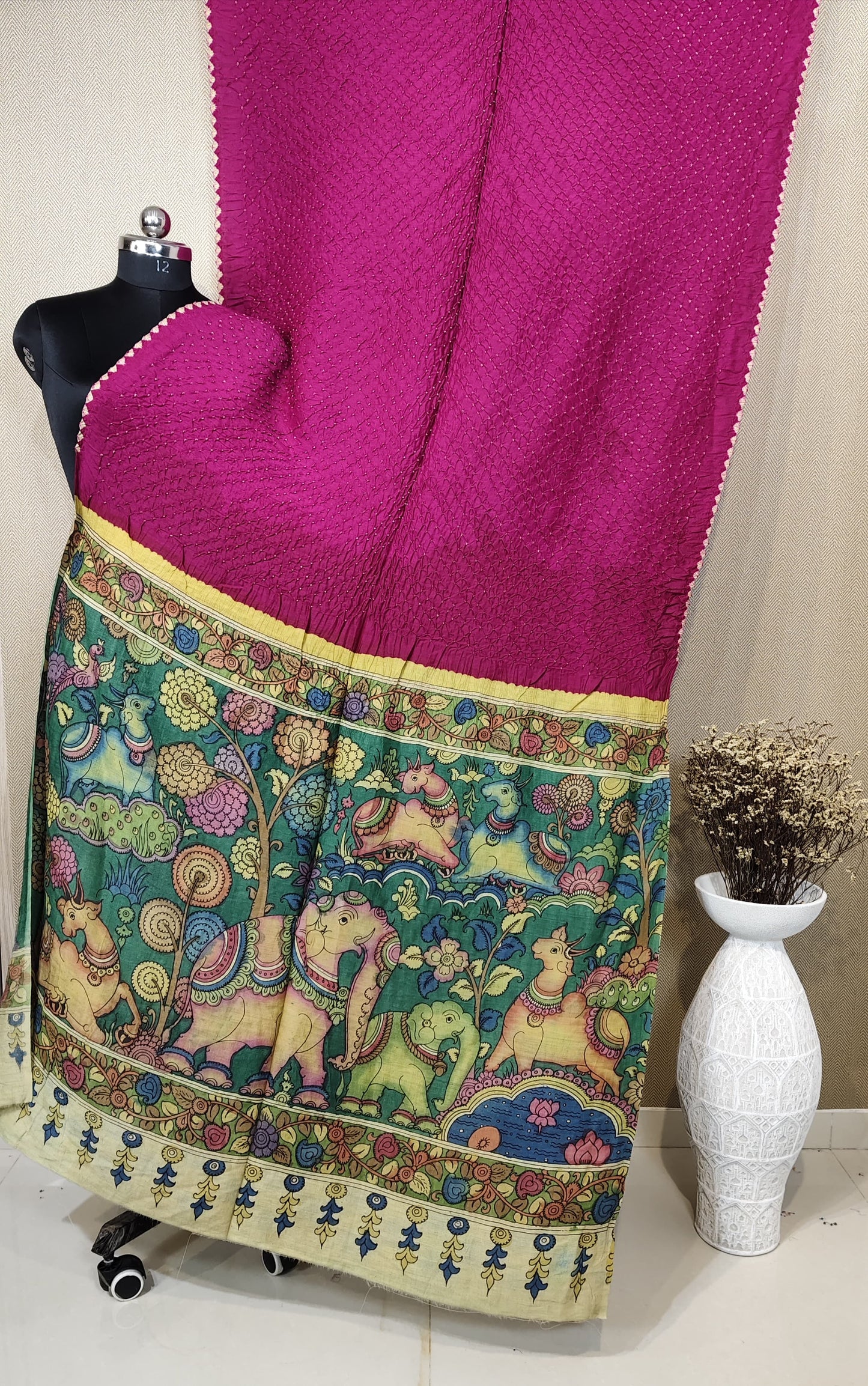 A magenta Munga silk Bandhani saree with a detailed, hand-painted Kalamkari pallu showcasing a vibrant scene of elephants and animals.