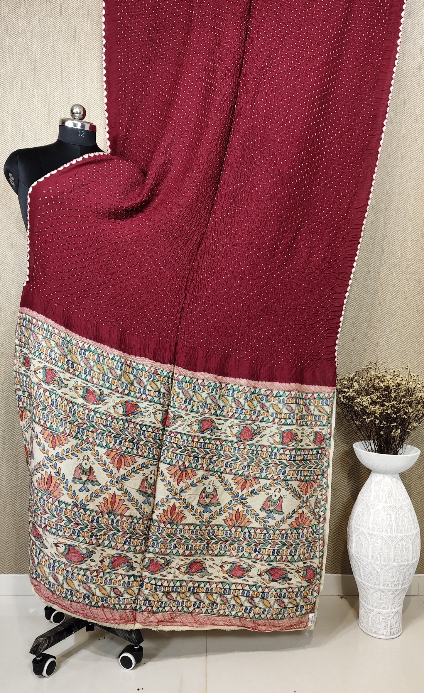 A deep maroon Munga silk Bandhani saree with a hand-painted Kalamkari pallu depicting rows of fish, lotus flowers, and traditional figures.