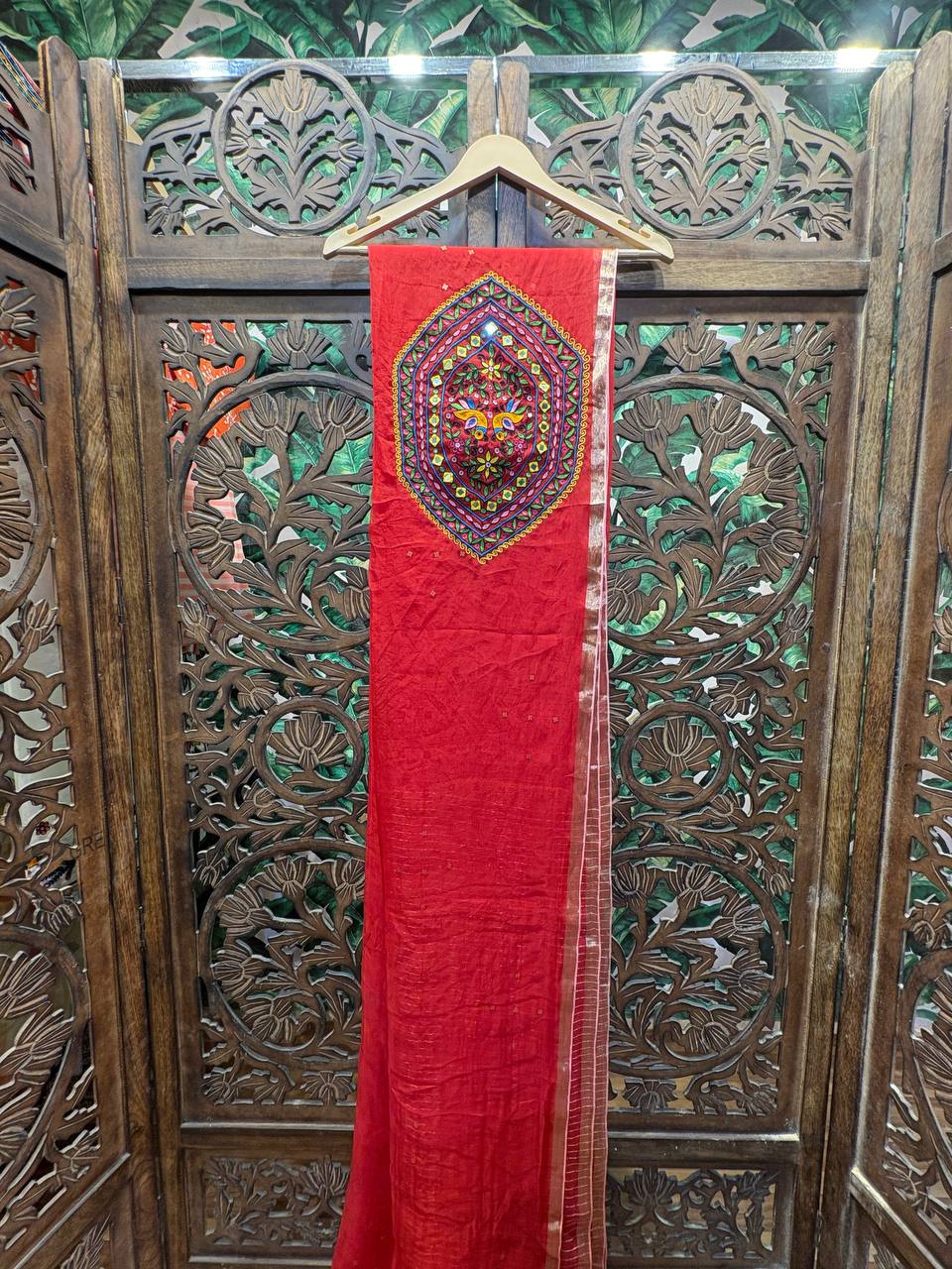Full view of the Ruhani red organza saree hanging on a hanger, showcasing the large Kutchi embroidery patch on the pallu.