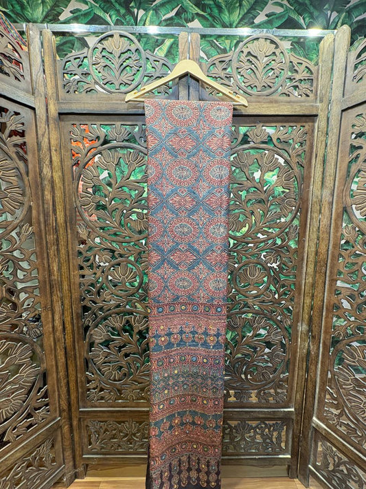 Full length view of the Mihira saree, a teal-blue and maroon Ajrakh saree with Lambani embroidery, hanging against a carved wooden screen.