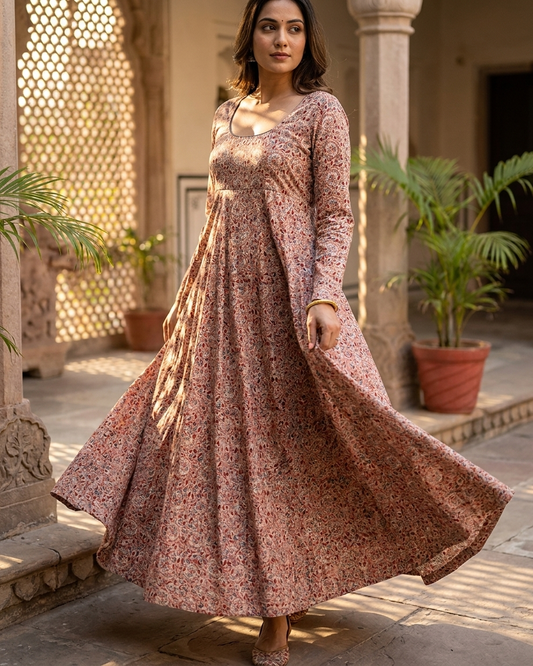 Woman in a long floral dress standing in an outdoor setting with plants and stone architecture.