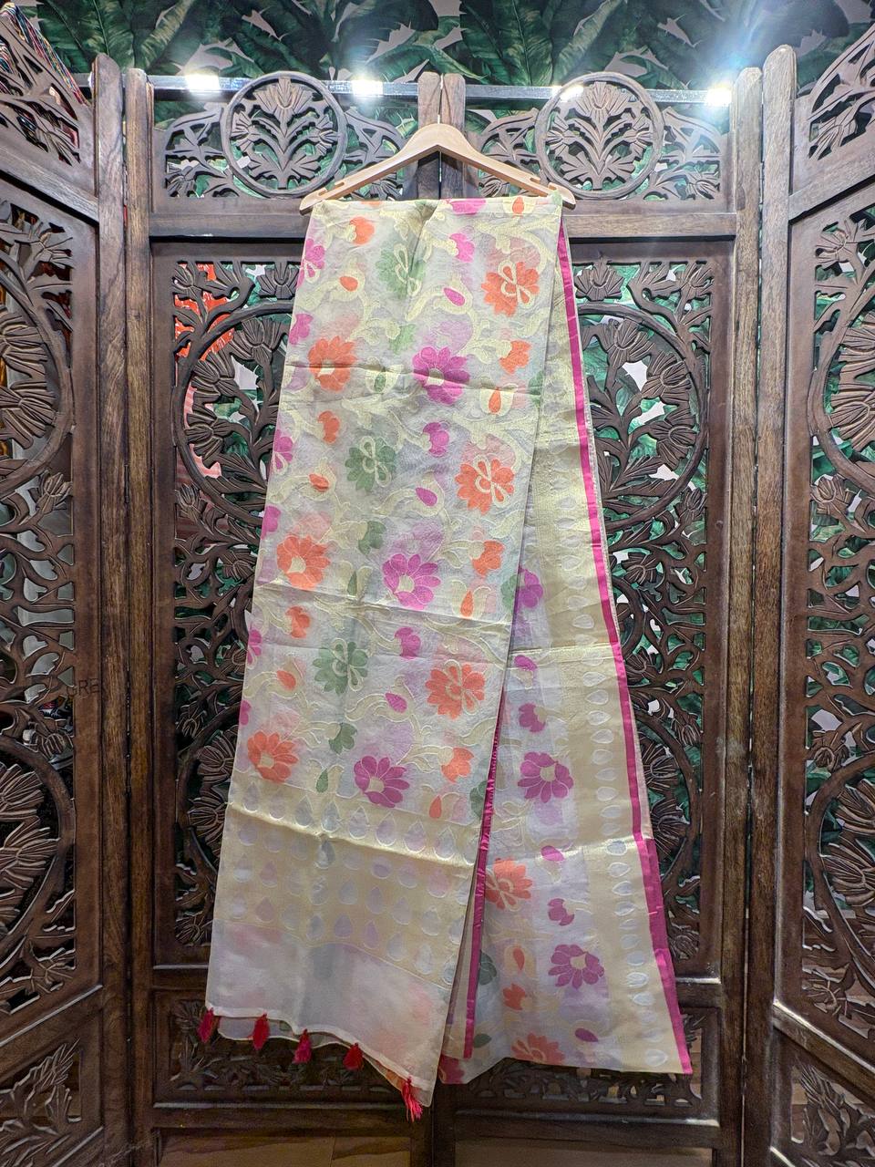 Full length view of a light gold Banarasi organza saree with pink, orange, and green floral meenakari work and a rani pink border.