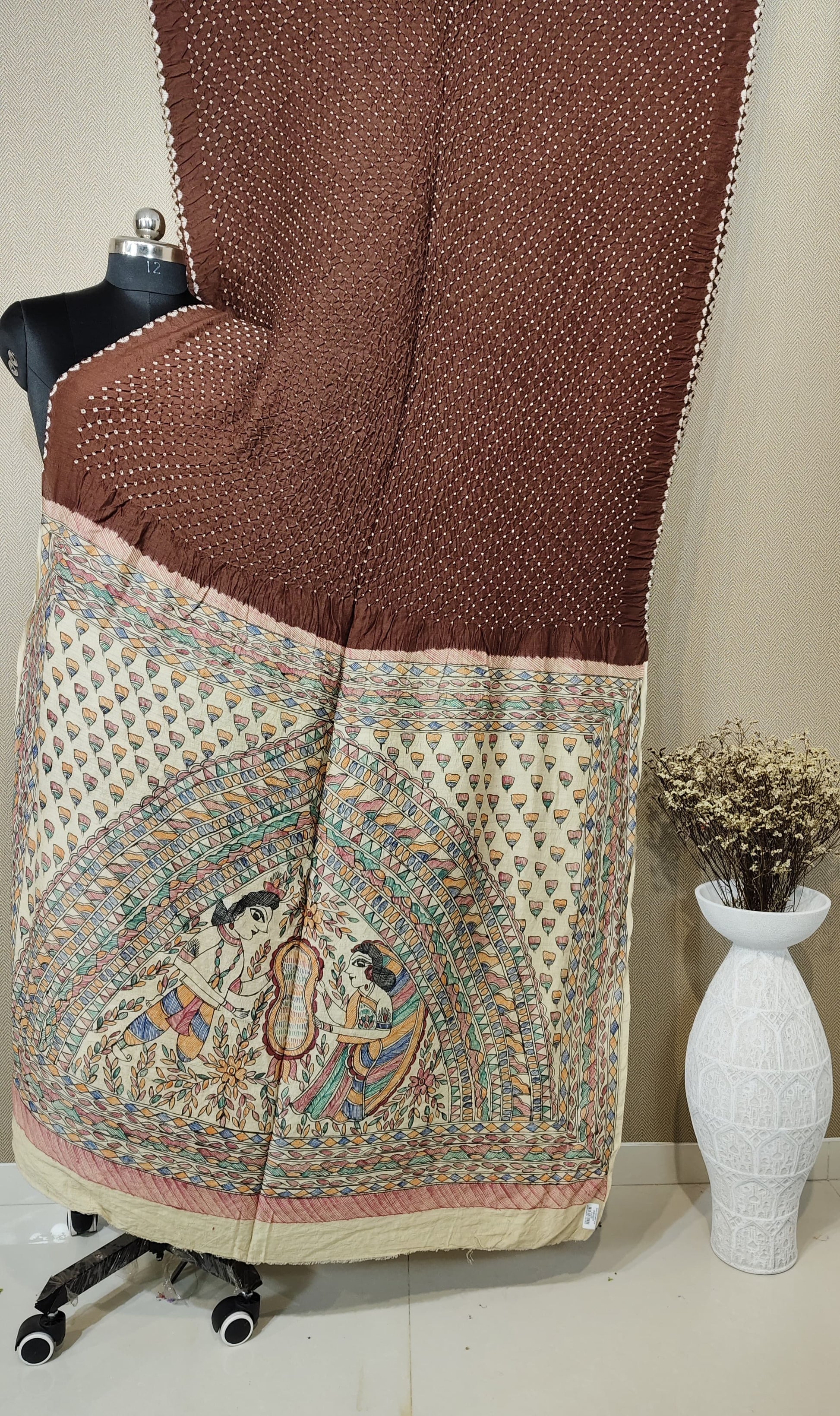 A unique brown Munga silk Bandhani saree with a hand-painted Kalamkari pallu illustrating a traditional scene with two female figures (Gopis).