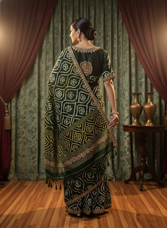 Woman in a black and white patterned saree standing in front of a curtain with a table and vases.