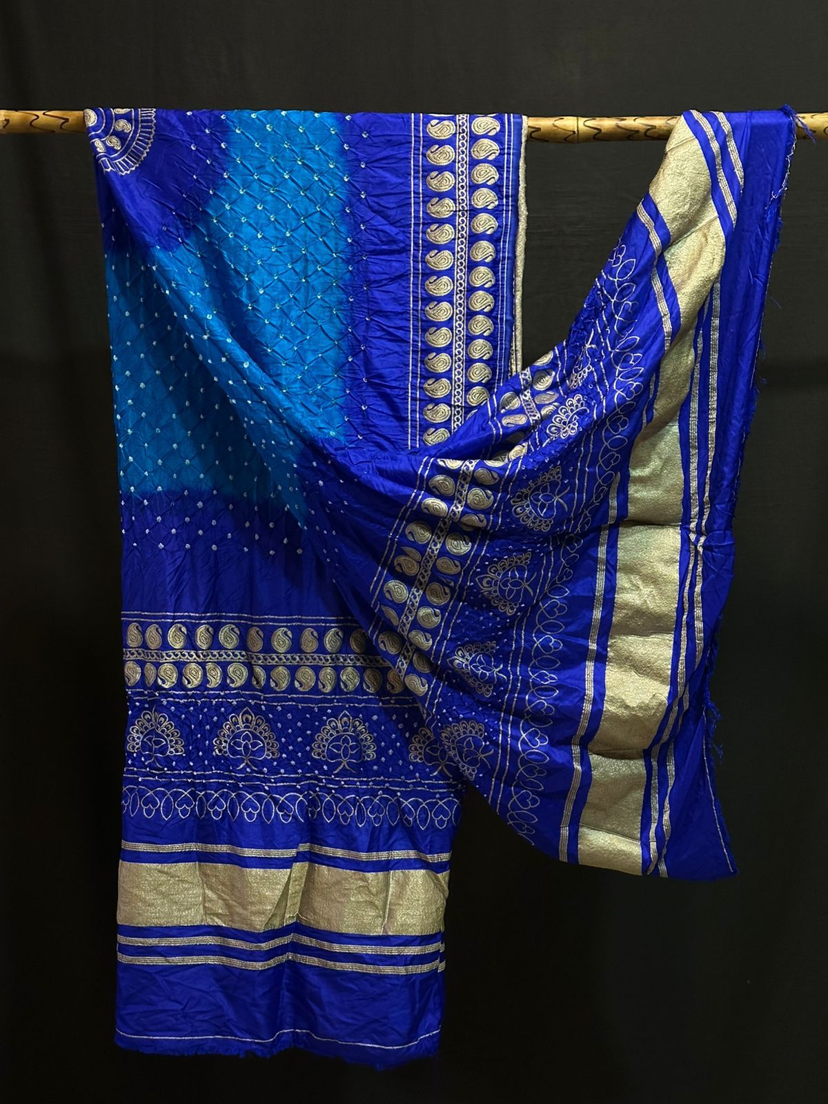 An elegant royal blue Gajji silk Bandhani dupatta with a two-tone tie-dye effect and a shimmering silver-toned Zari border with peacock motifs.