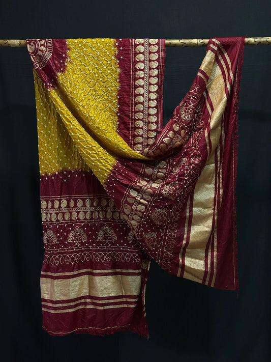A handcrafted Gajji silk Bandhani dupatta in mustard yellow and maroon, featuring intricate tie-dye work and a heavy gold Zari border.