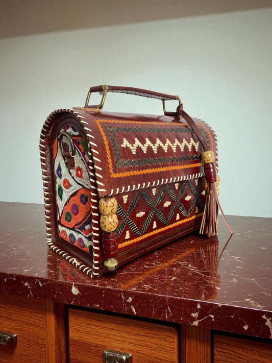 Ethnic handcrafted leather trunk bag with tribal embroidery and a top handle, placed on a carved wooden table.