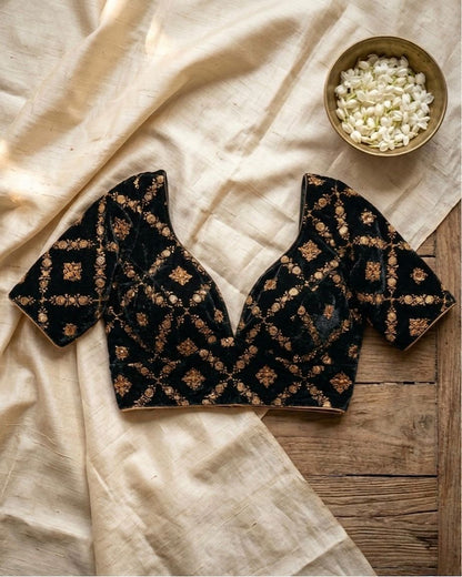 Black embroidered top on a wooden surface with a bowl of white flowers.