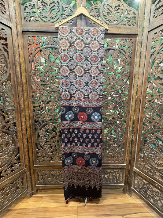 Full view of the Ishani Ajrakh Hand Block Printed Modal Silk Saree in indigo and maroon, hanging on a hanger against a carved wooden screen.